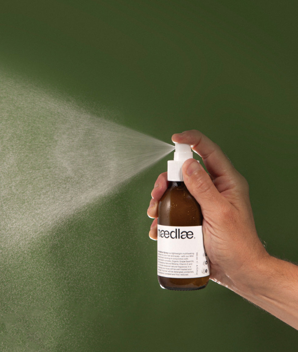 Hand holding Naedlae Foundation Spray natural leave in conditioner spray against green background